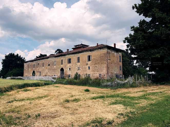 Una vecchia cascina in un campo, con pareti in mattoni e un cielo nuvoloso.