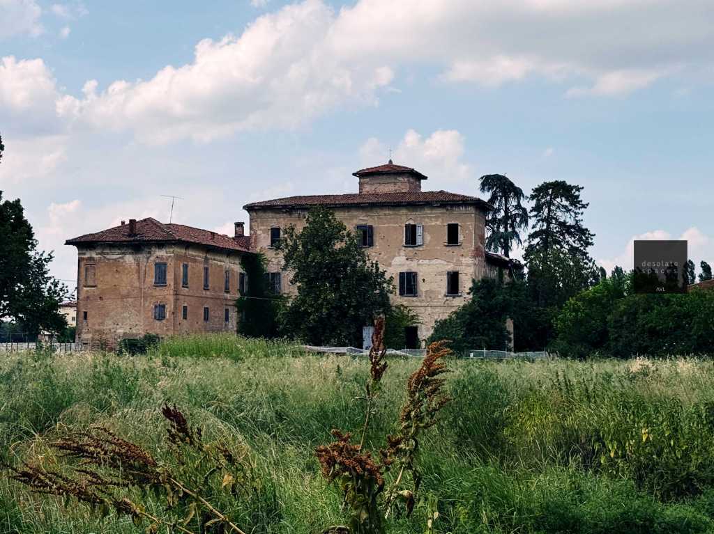 Un antico edificio abbandonato circondato da un prato verde e alberi.
