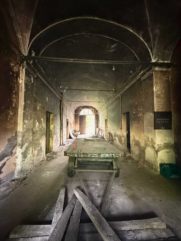 Corridoio desolato con una carriola al centro, luci soffuse e pareti danneggiate.