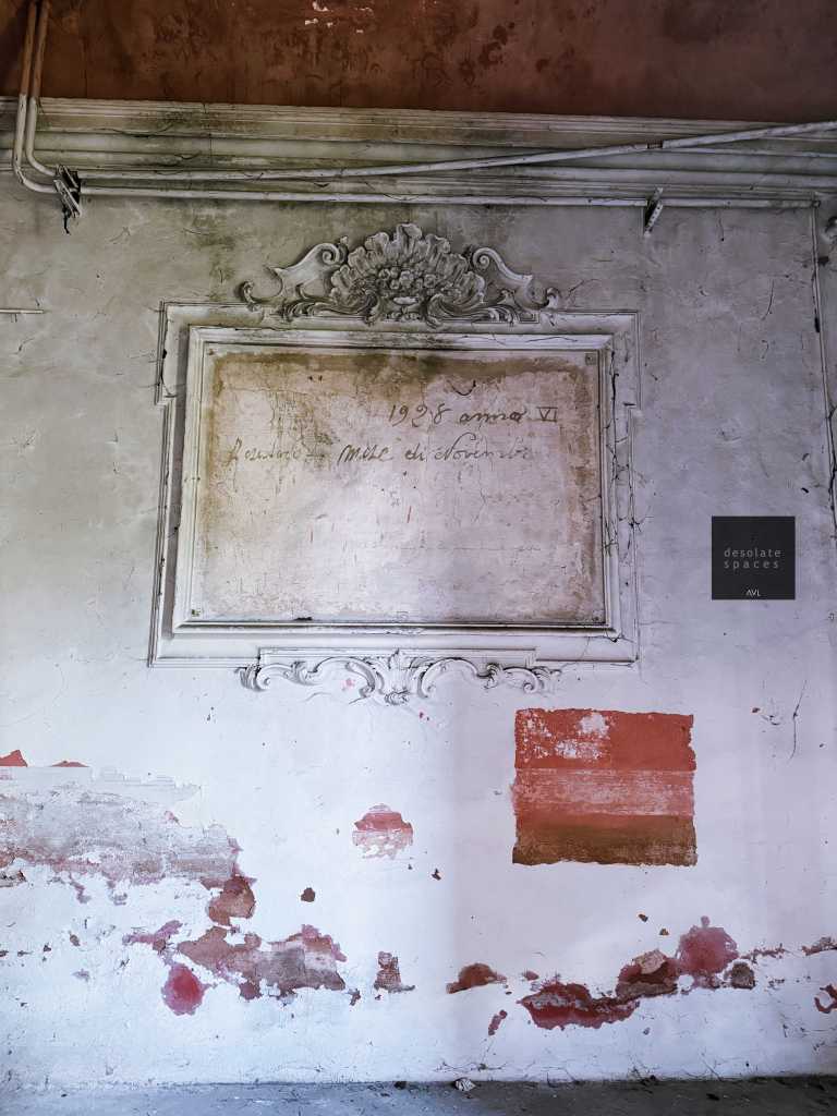 Parete interna con cornice decorativa e scritta antica che indica l'anno 1958, con segni di umidità e peeling della vernice.