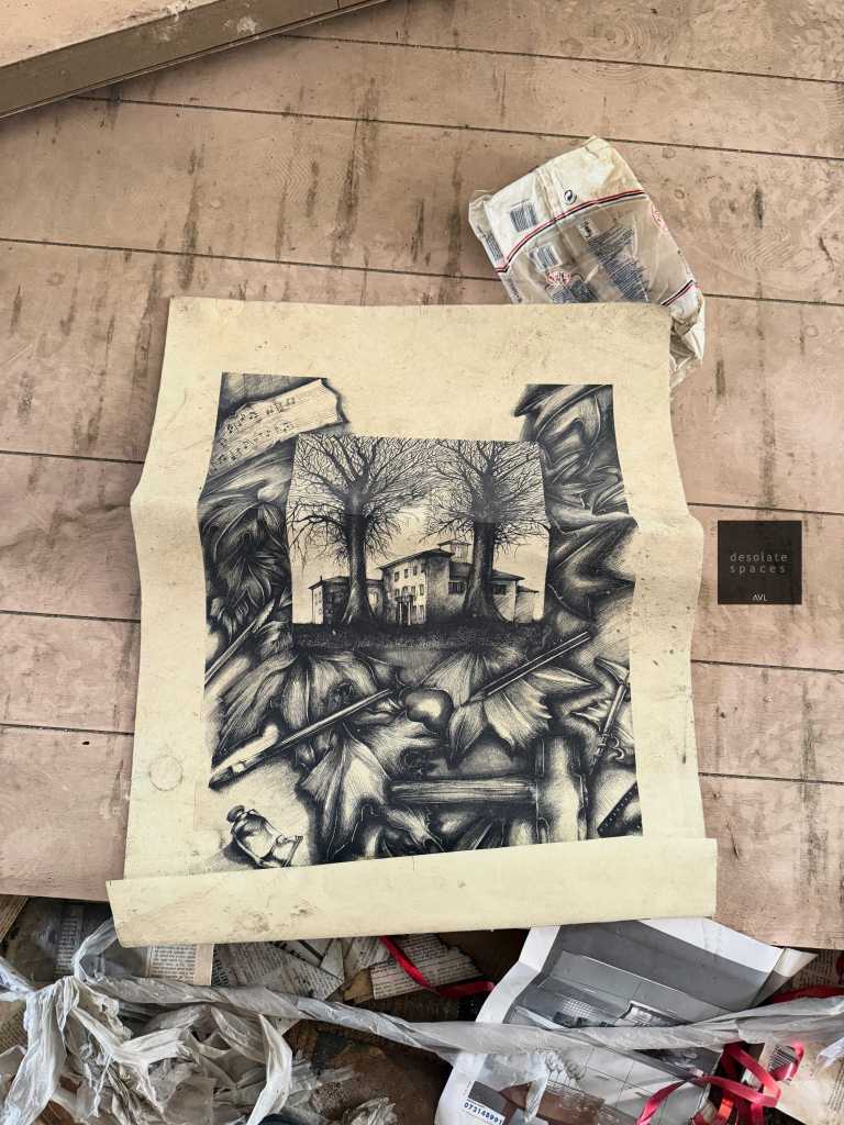 Un disegno artistico realizzato su carta, raffigurante alberi e una casa, posato su un pavimento sporco tra rifiuti e carta straccia.
