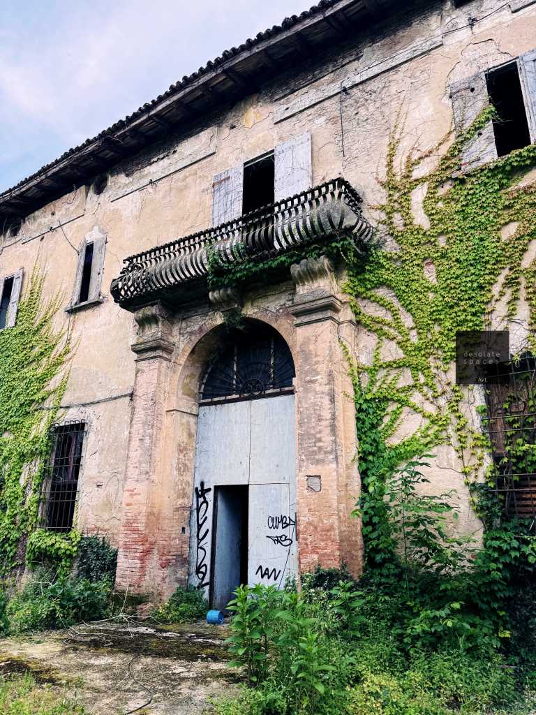 Facciata di un edificio abbandonato con tracce di graffiti e vegetazione che cresce sulle pareti.