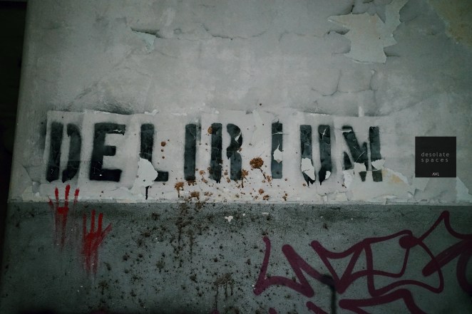 Scritta su muro che dice 'DELIRIUM', con vernice scrostata e macchie di ruggine.