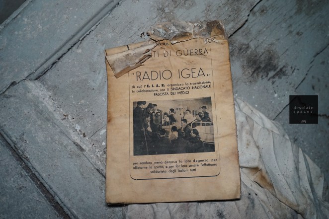 Un vecchio volantino di Radio Igea, con un'immagine di persone in un ambiente radiofonico, giace su un pavimento polveroso.