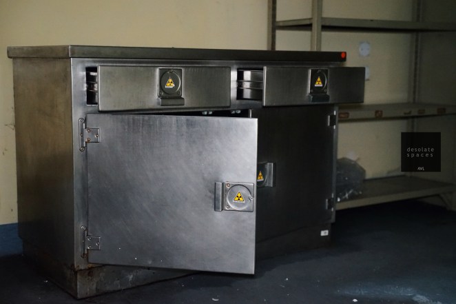 Un armadietto metallico con tre cassetti e una porta aperta, dotato di simboli di avvertimento radioattivo.